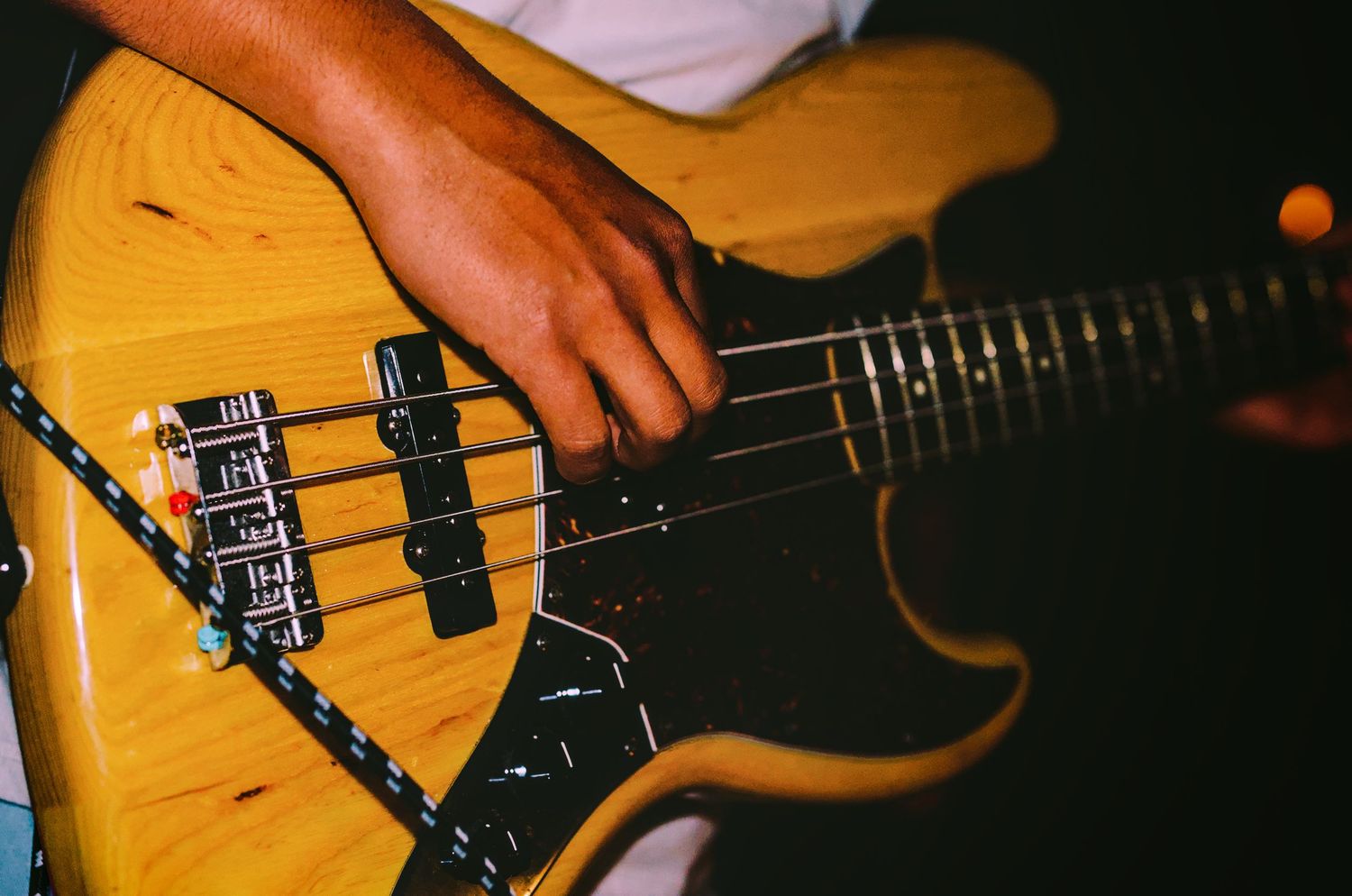 Close-up shot of hands playing a yellow bass guitar on stage under warm lighting.