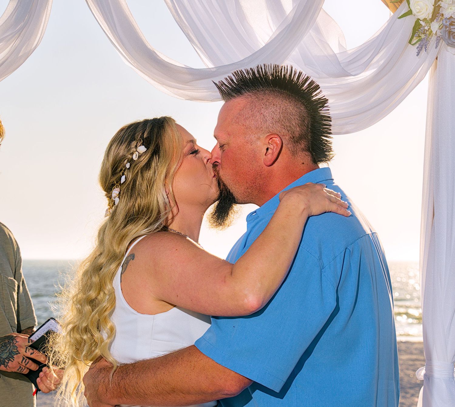A couple sharing their first kiss as newlyweds during a beach wedding ceremony.
