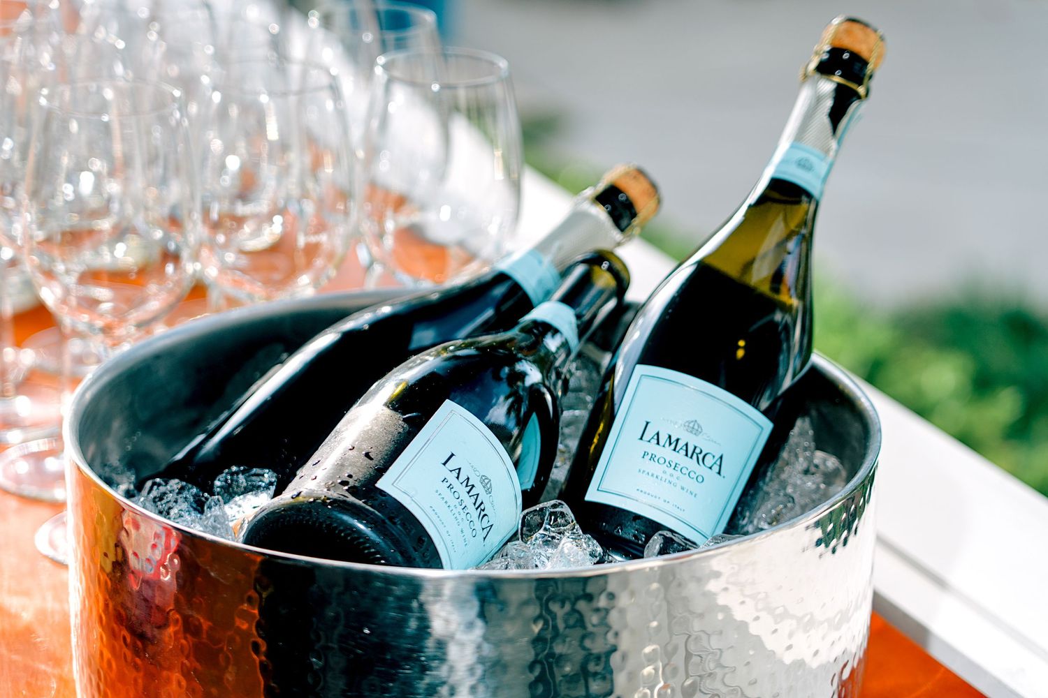 La Marca Prosecco bottles chilling in an ice bucket with wine glasses at an outdoor event.