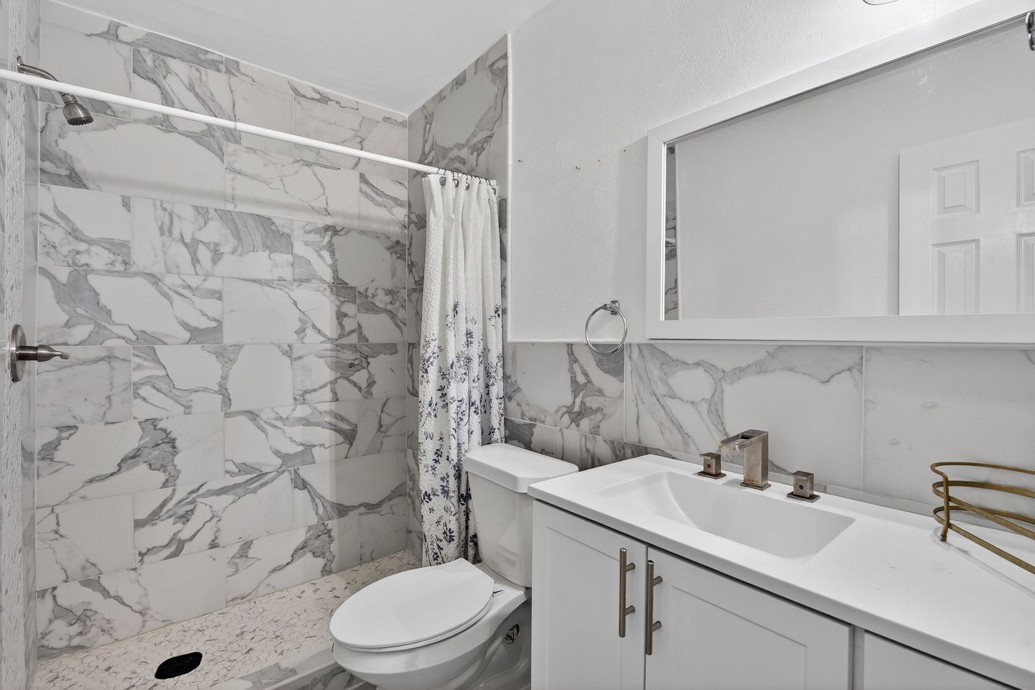 Modern bathroom interior with marble-look tile shower surround, white vanity, and chrome fixtures in neutral color scheme.