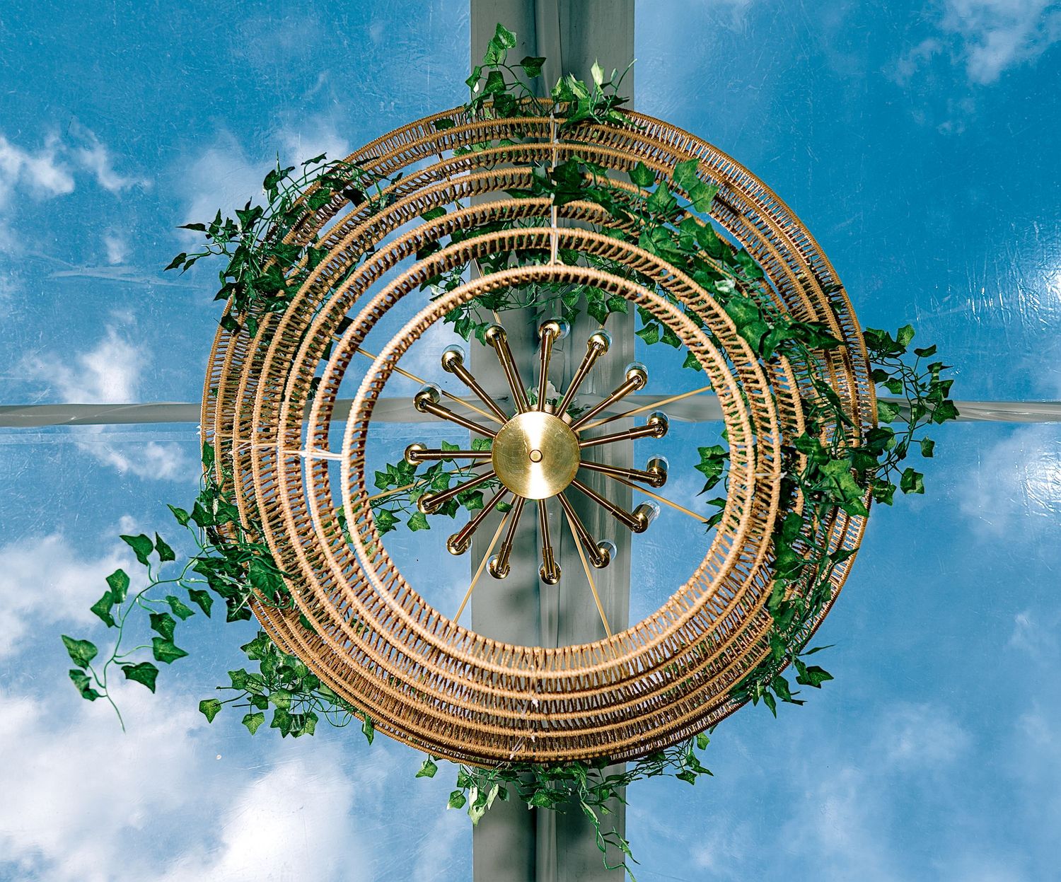 A decorative circular wreath with green ivy and gold sunburst centerpiece against a blue sky.