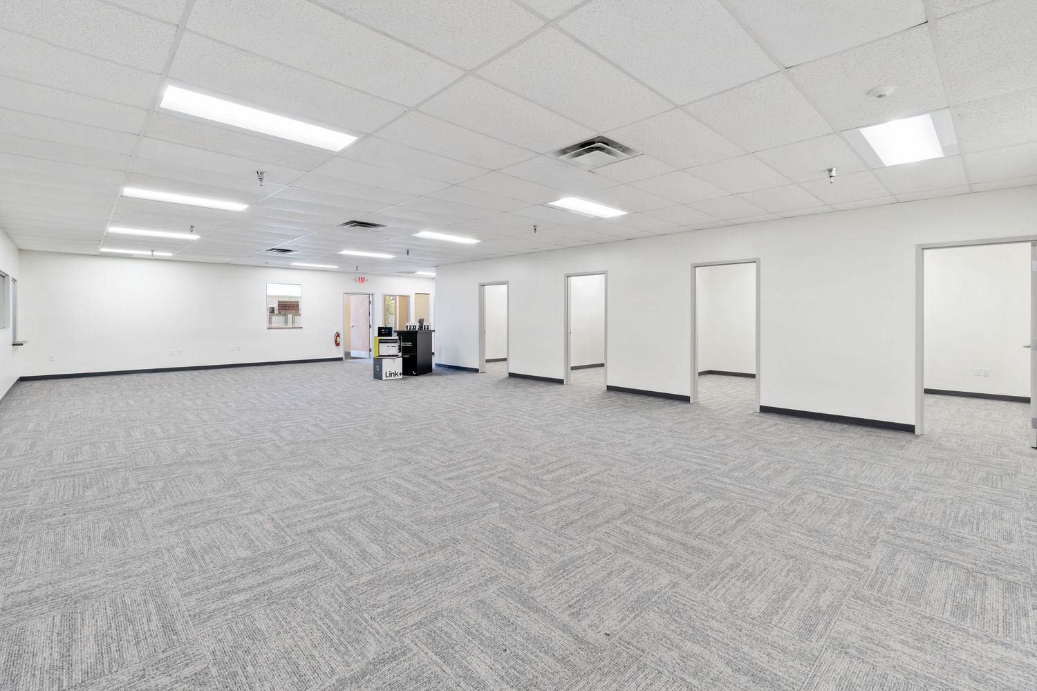 Empty modern office space with gray carpeting, white walls, fluorescent lighting and multiple doorways.