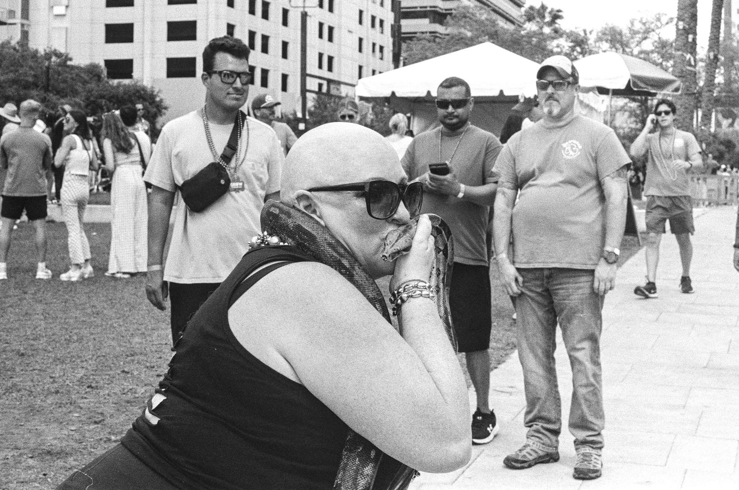 Person crouching to take a photo at an outdoor event with people standing in background, black and white photography.