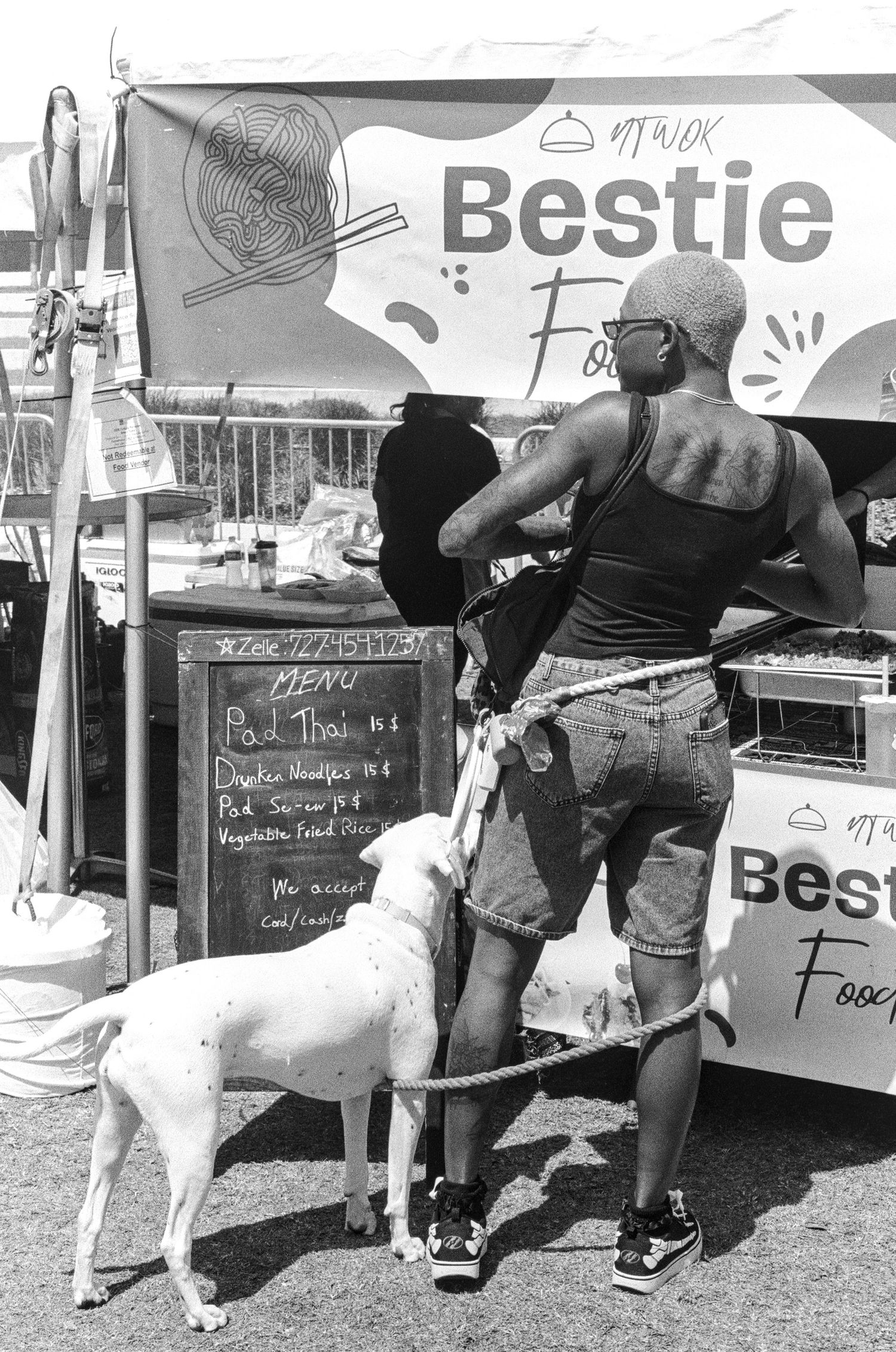 Person with dog ordering food at Bestie Food Truck outdoor market, black and white photo.