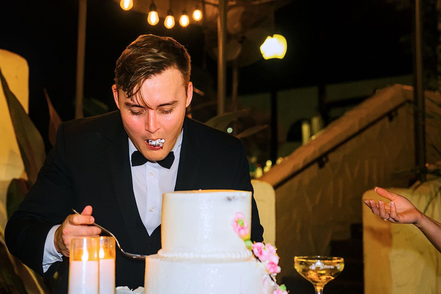 Wedding celebration at night with guests gathered around tables under ambient lighting.