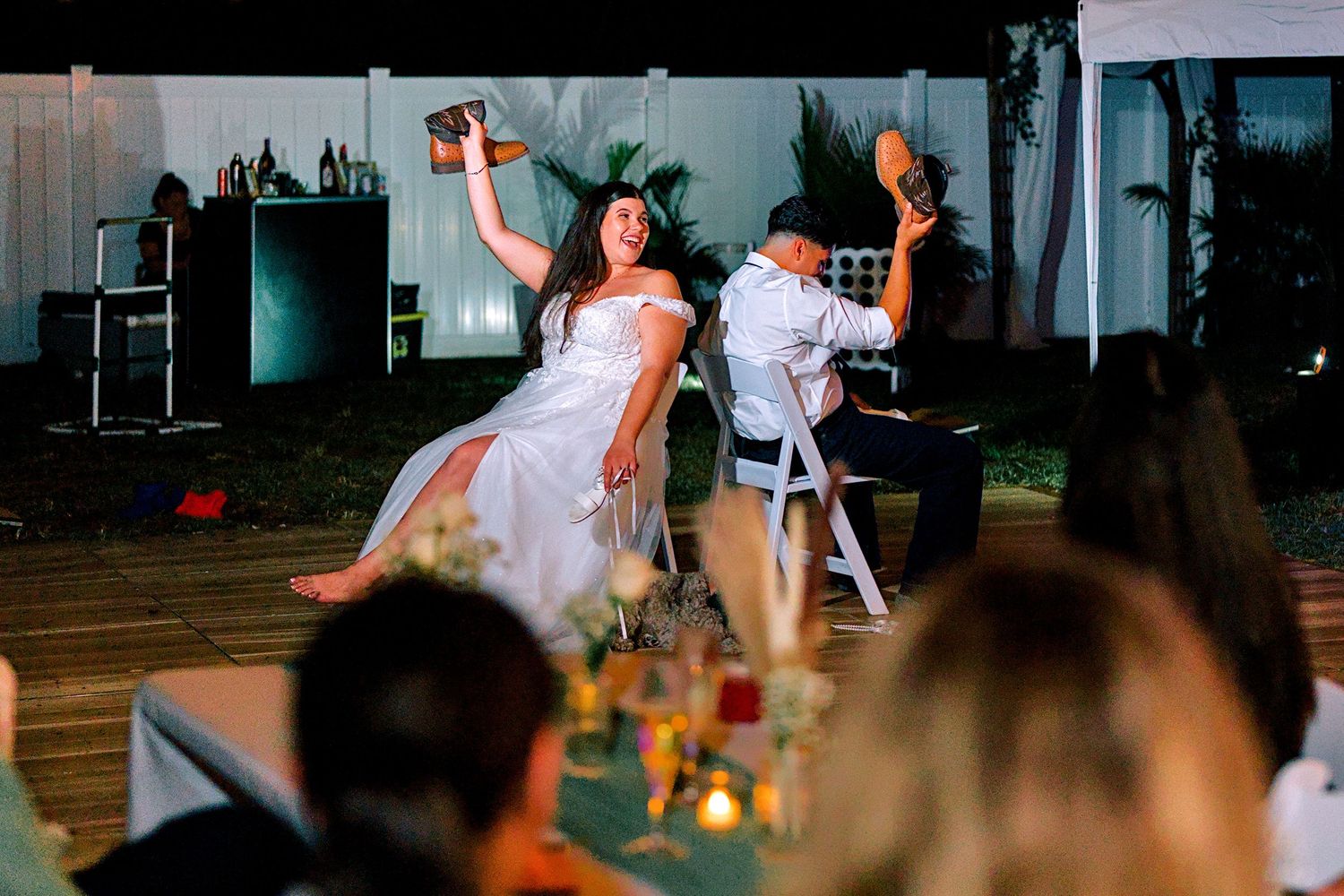 Bride laughing joyfully during a fun wedding reception game outdoors at night with guests watching.