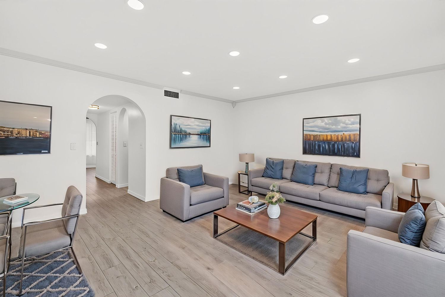 Modern living room with gray furniture, wood flooring, and coastal artwork features arched doorway and recessed lighting.