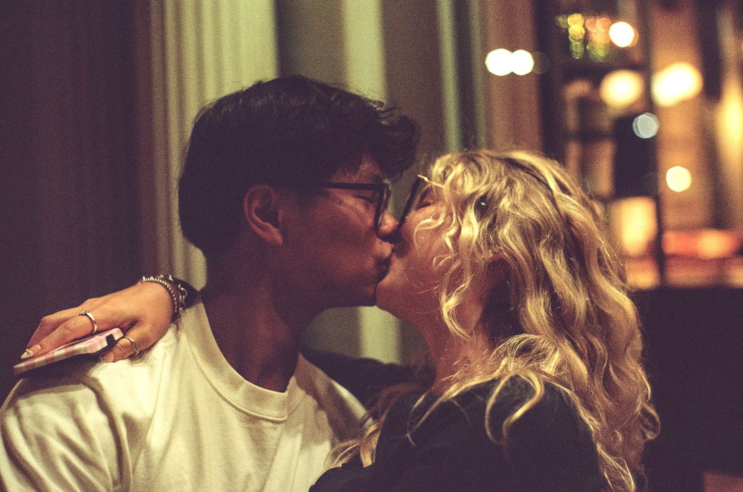 Young couple sharing a romantic kiss at night with bokeh lights in the background.