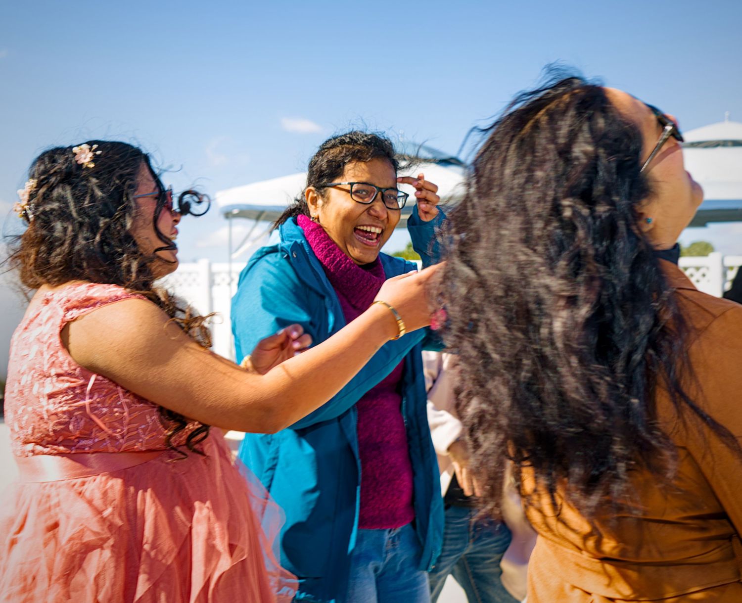 A group of friends laugh and dance together outdoors on a bright sunny day with blue skies in the background.