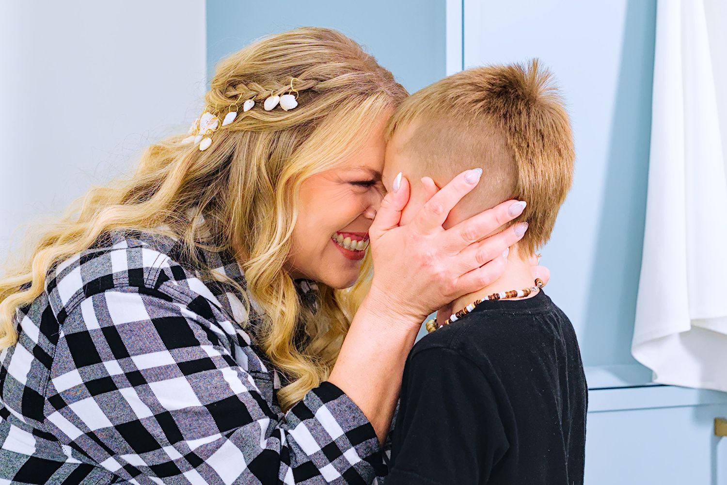 A couple in black and white plaid shirts share a joyful moment together against a light blue background.