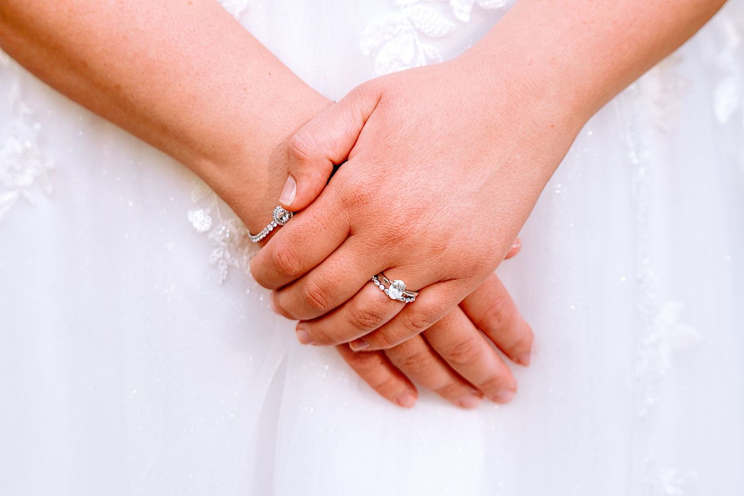 Close-up of bride and bridesmaid holding hands showing elegant wedding and engagement rings.