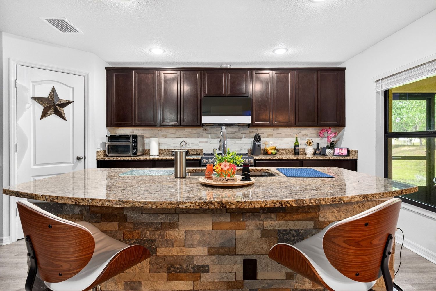 Modern kitchen with dark wood cabinets, granite island, stone backsplash, stainless appliances, and bar seating area.