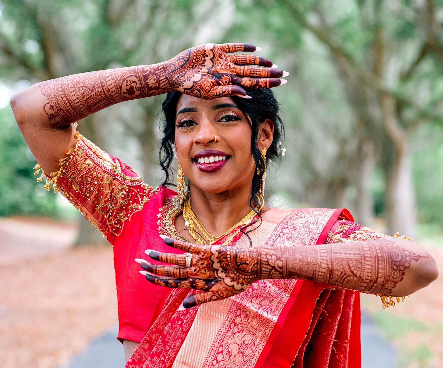 Indian bride in red saree displaying intricate henna mehndi designs on hands outdoors.