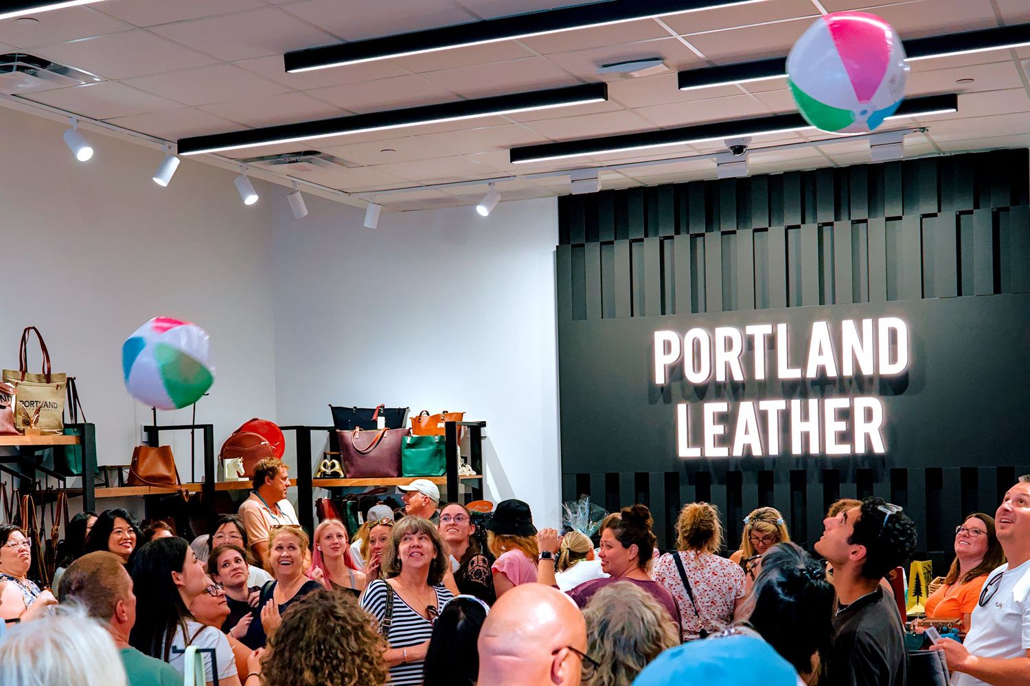Crowded Portland Leather store grand opening event with colorful beach balls floating above excited shoppers.