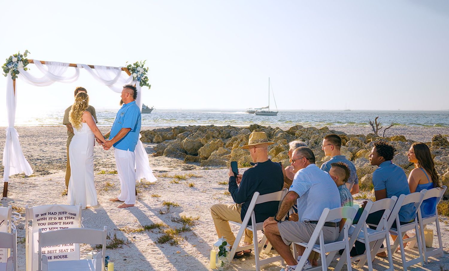 Beachside wedding ceremony setup with guests seated facing a floral arch and ocean view.