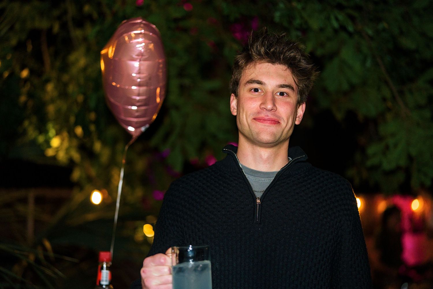 A person holds a heart-shaped balloon at a nighttime outdoor celebration.