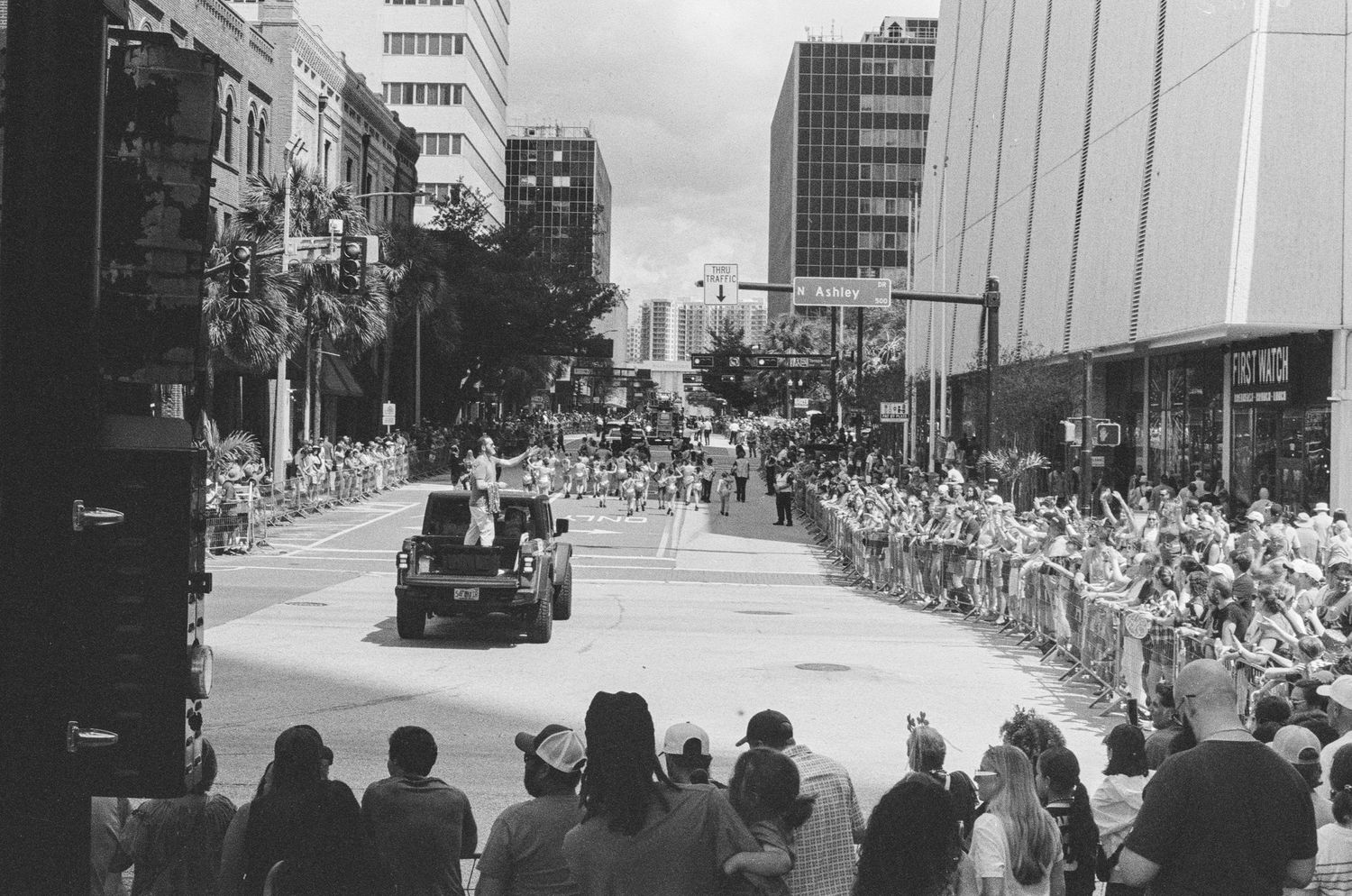 Black and white photo of a large crowd lining a city street during a parade with tall buildings in background.