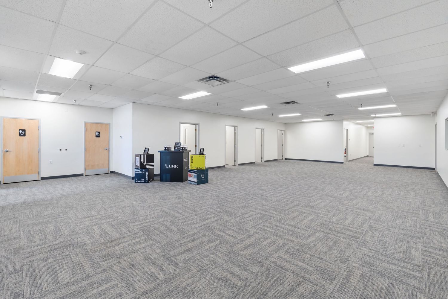 Empty commercial office space with fluorescent lighting and gray carpet showing multiple angles of the open floor plan.