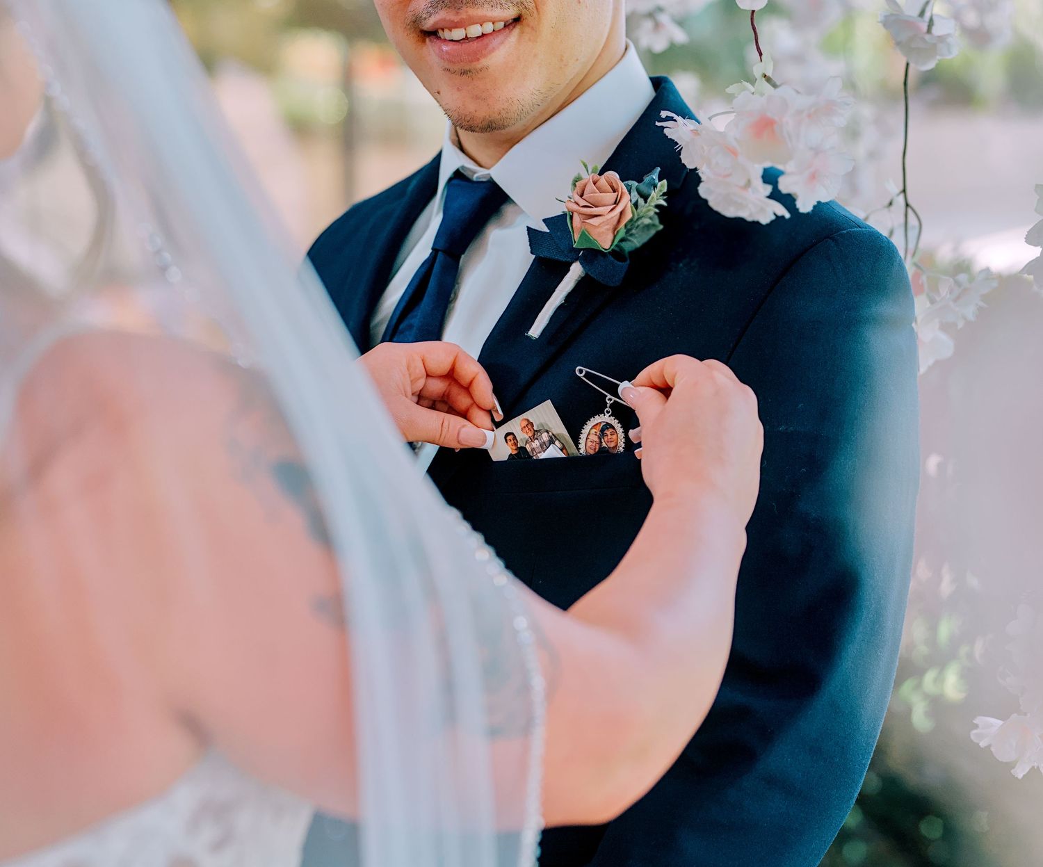A groom in a navy suit receives a sentimental keychain gift during an outdoor wedding ceremony.