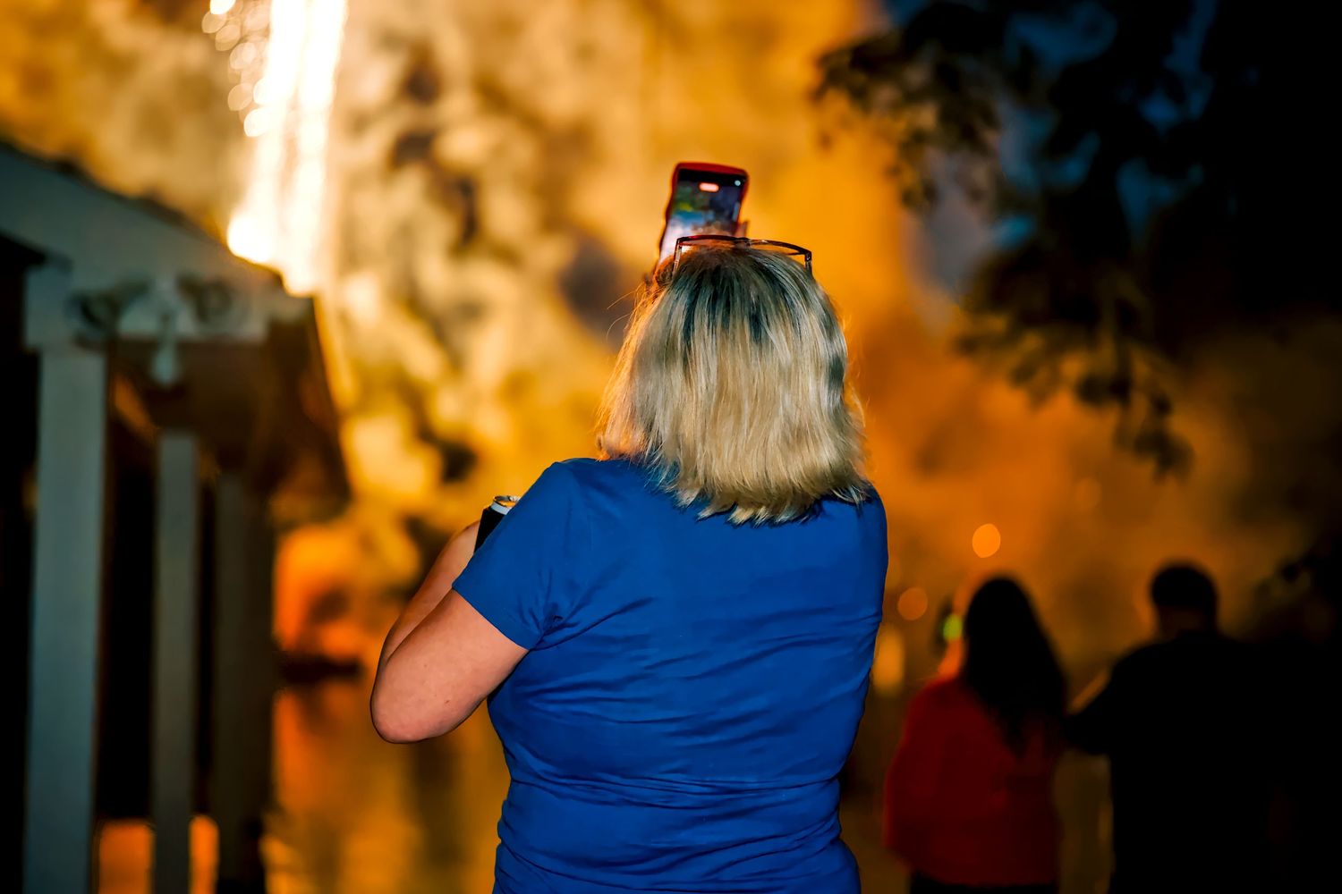 Woman with phone on head watches fireworks display at night outdoor event.