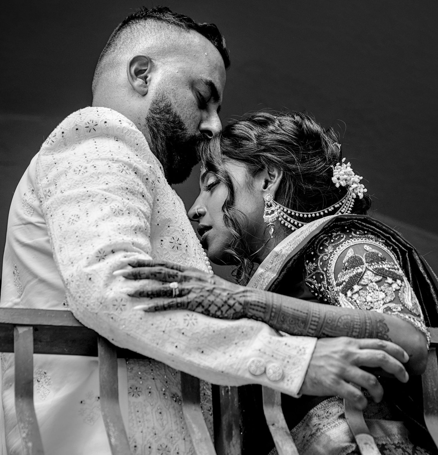 Black and white photo of an Indian bride and groom in traditional wedding attire sharing a romantic embrace.