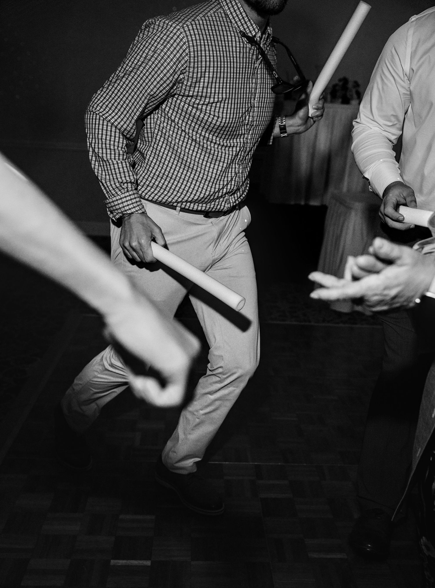 Men in formal attire holding batons dancing at an event, captured in black and white photography.