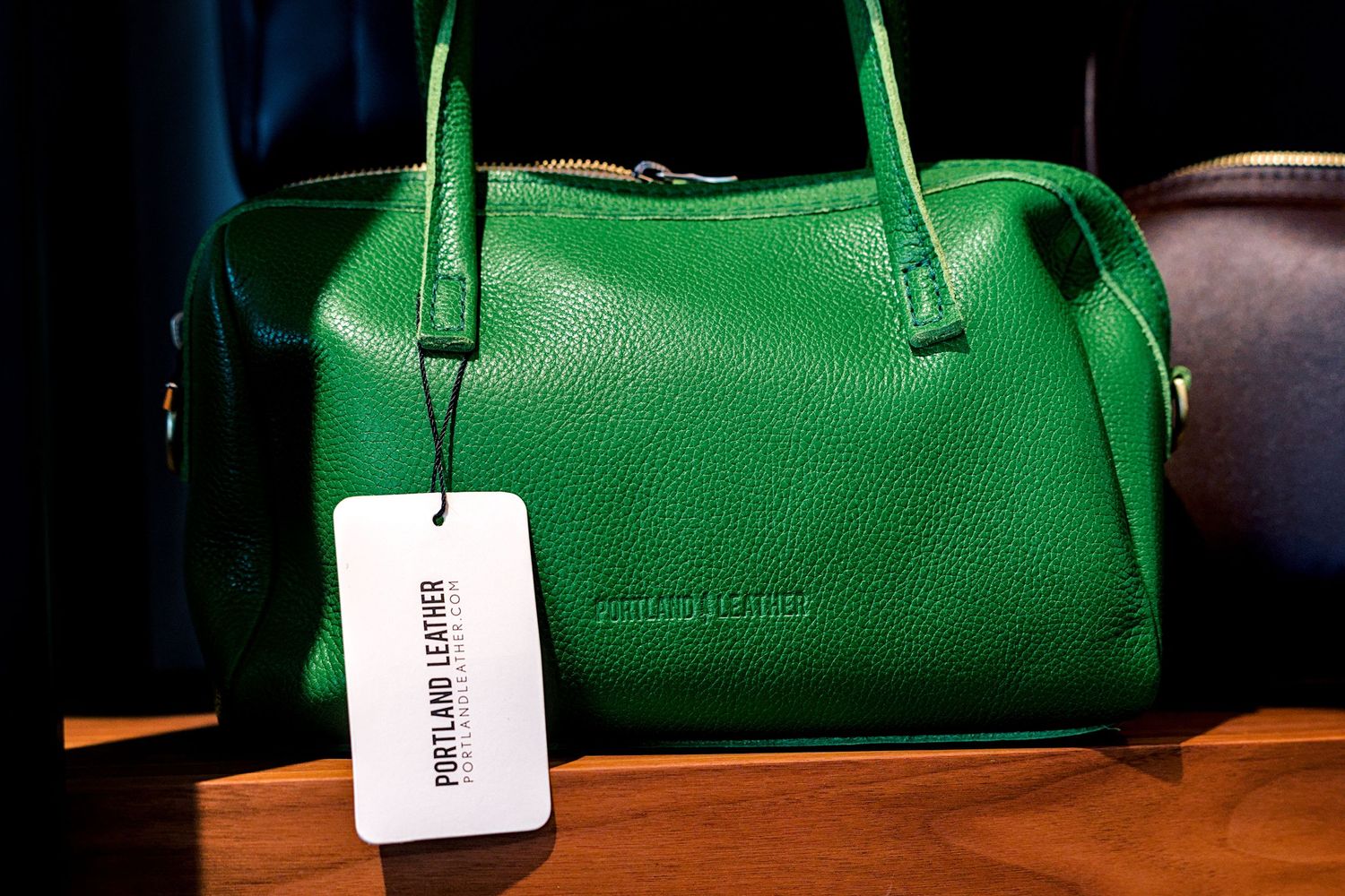 Green leather Portland Leather handbag with tag displayed on wooden surface.