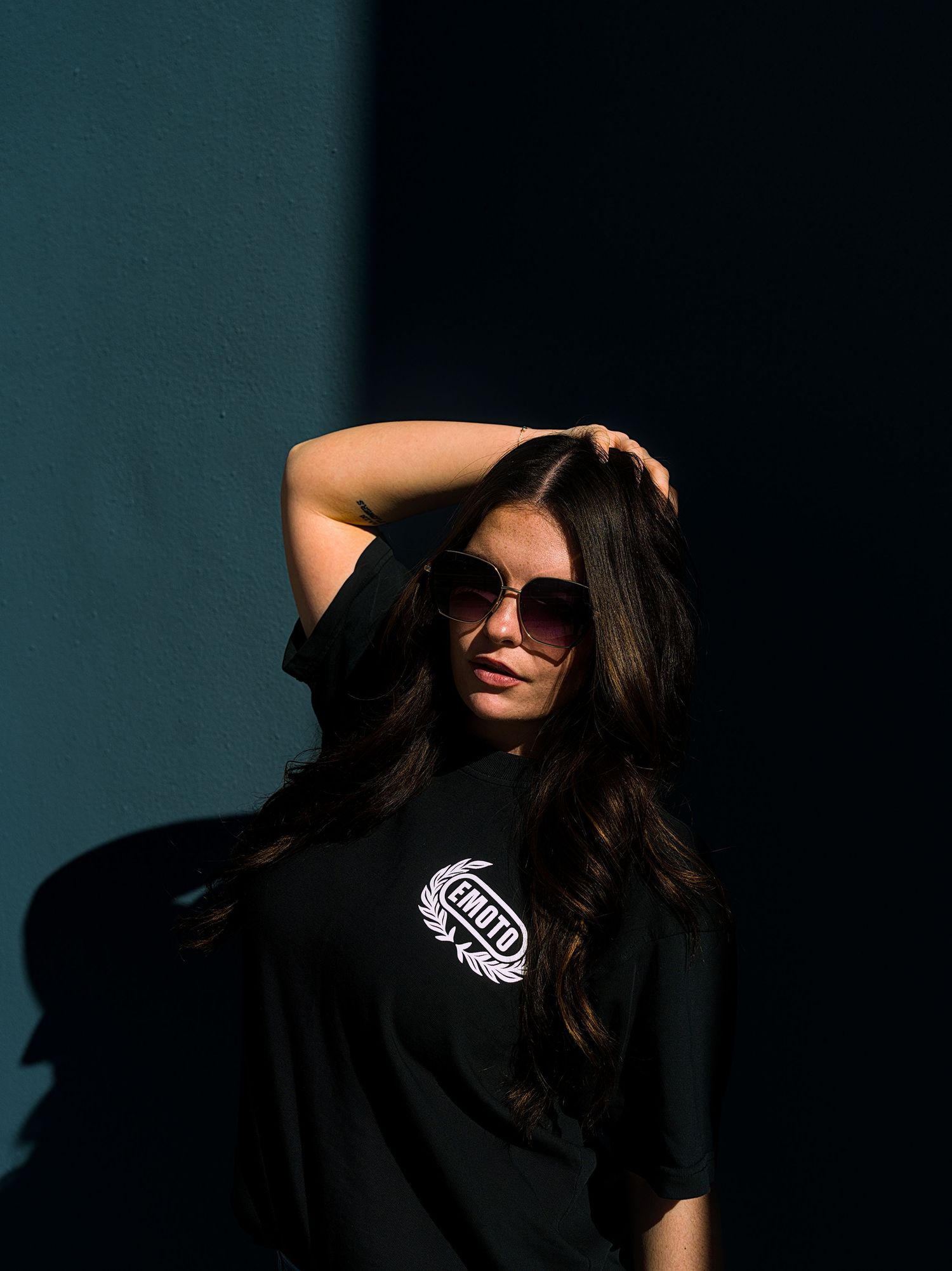 A silhouetted figure in a black t-shirt with a logo poses dramatically against a dark background.