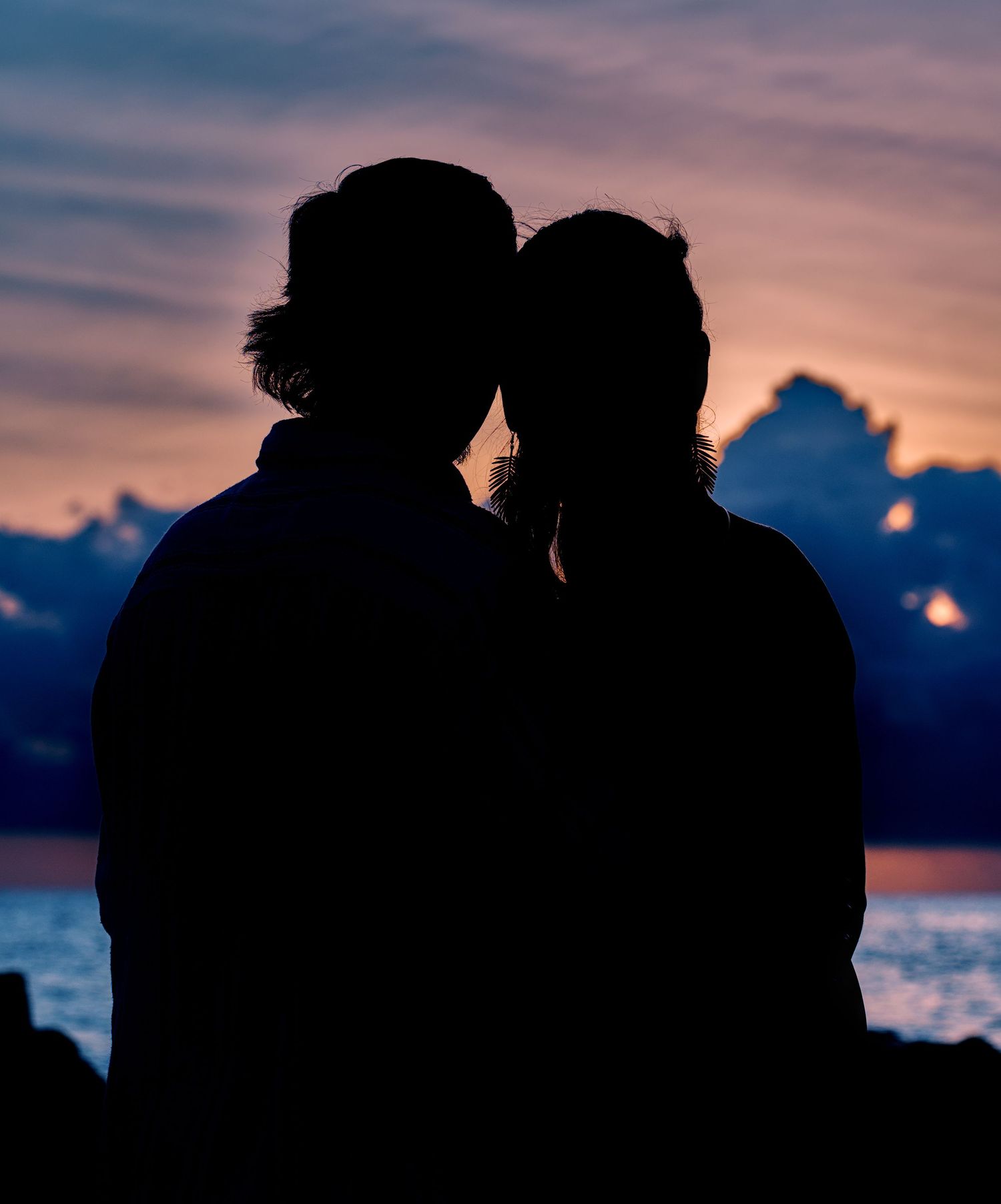 Silhouette of a romantic couple sharing a kiss against a stunning purple and orange sunset sky over the ocean.