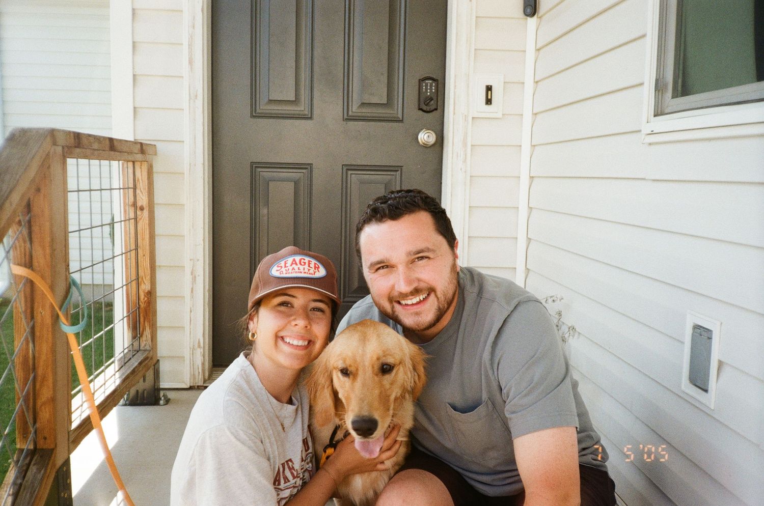 A golden retriever dog sits on a front porch with people in a casual home setting.