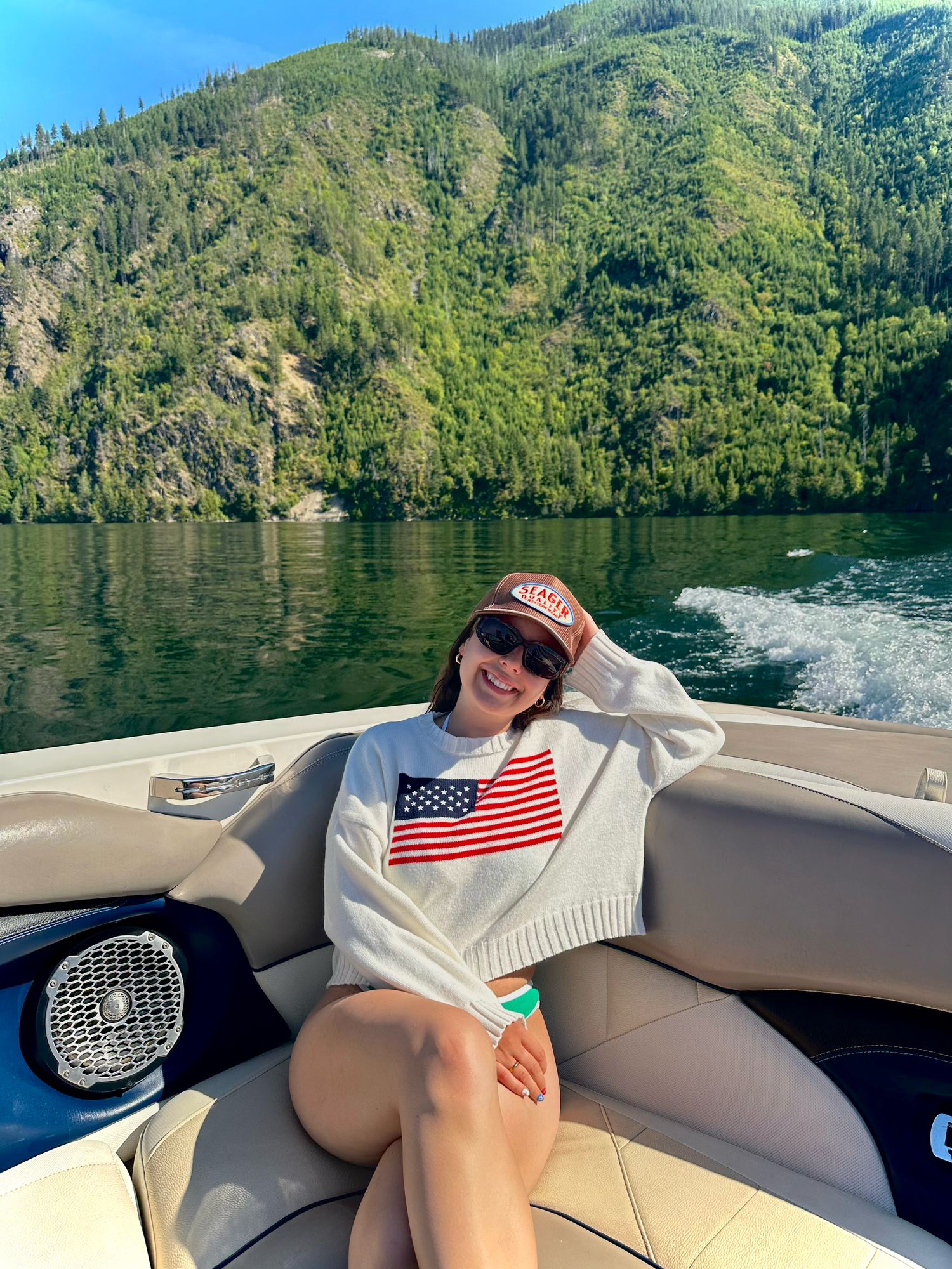 People relaxing on a boat with an American flag against mountainous lake scenery.