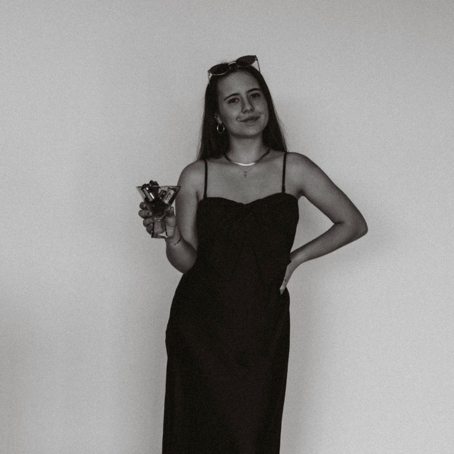 Black and white portrait of someone in an elegant black dress holding a wine glass against a plain background.