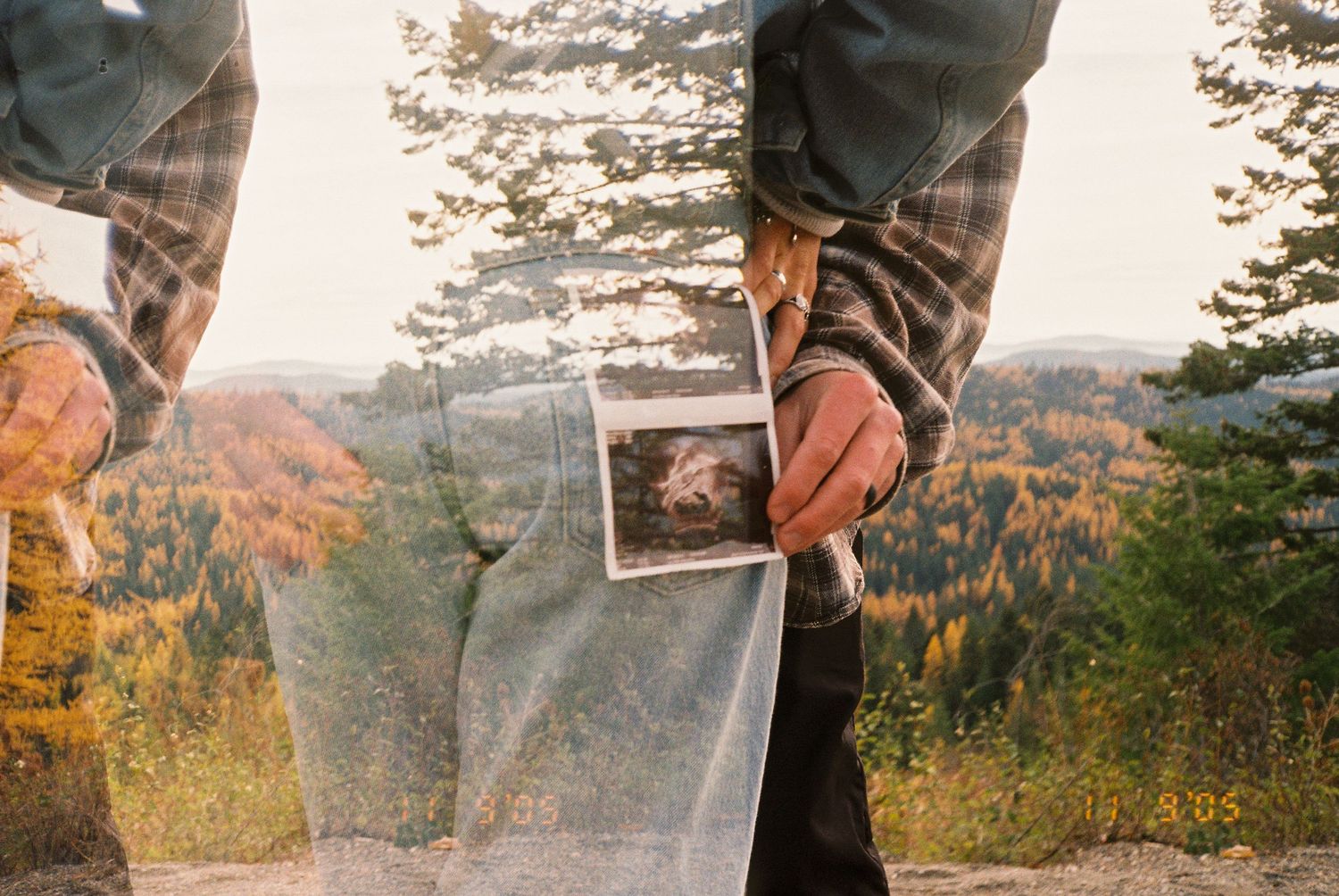 Couple holding ultrasound photo outdoors with autumn forest backdrop in double exposure film photograph.