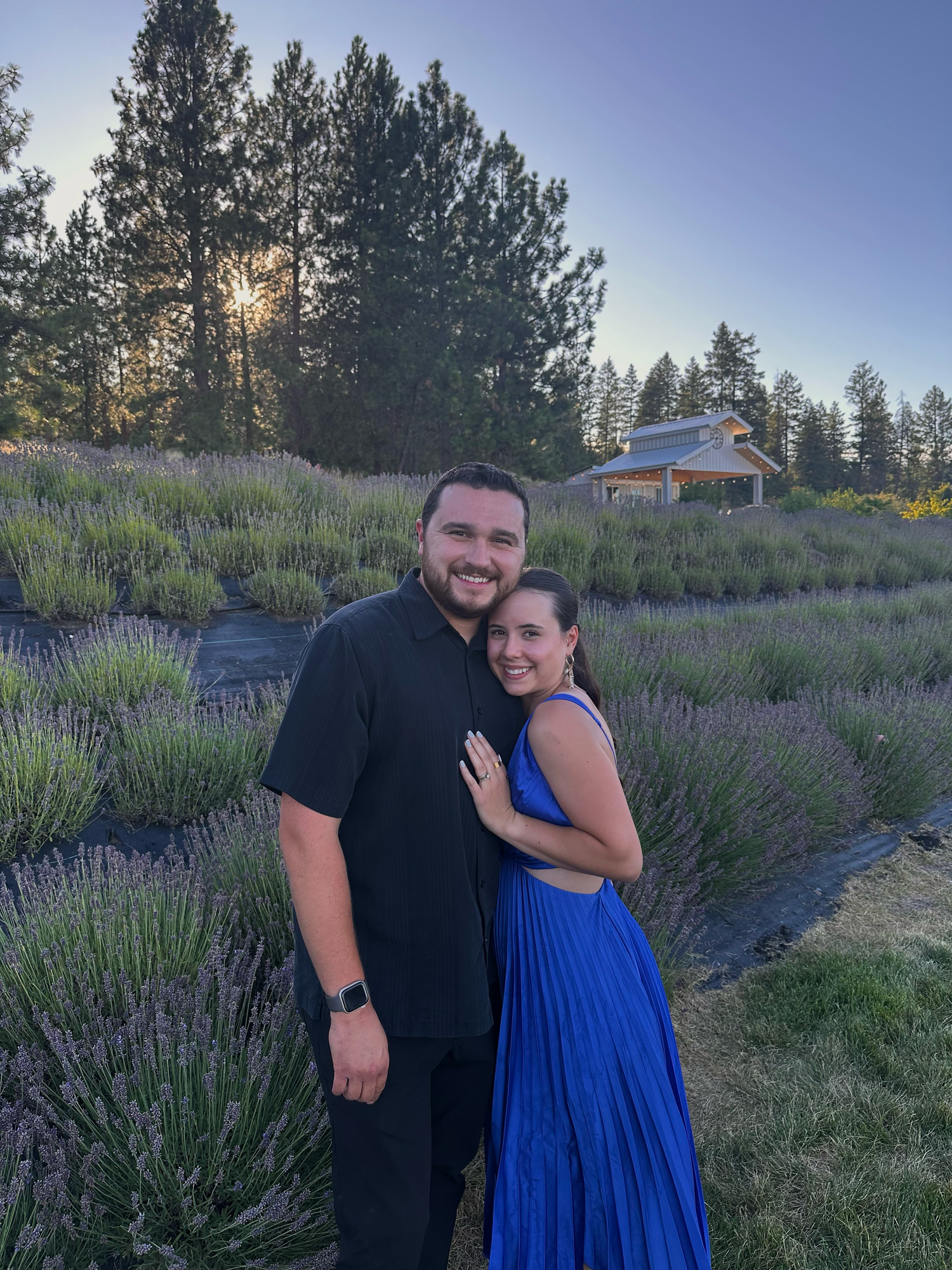 A couple poses together in a field of blooming purple lavender at sunset.