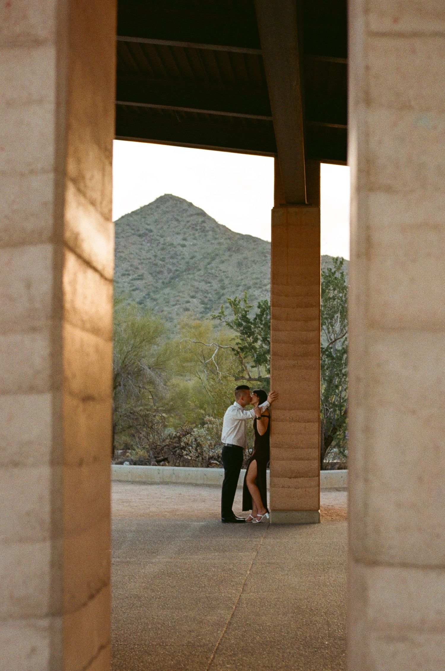 Couple embracing by a stone column with a desert mountain backdrop at an outdoor venue in Arizona.