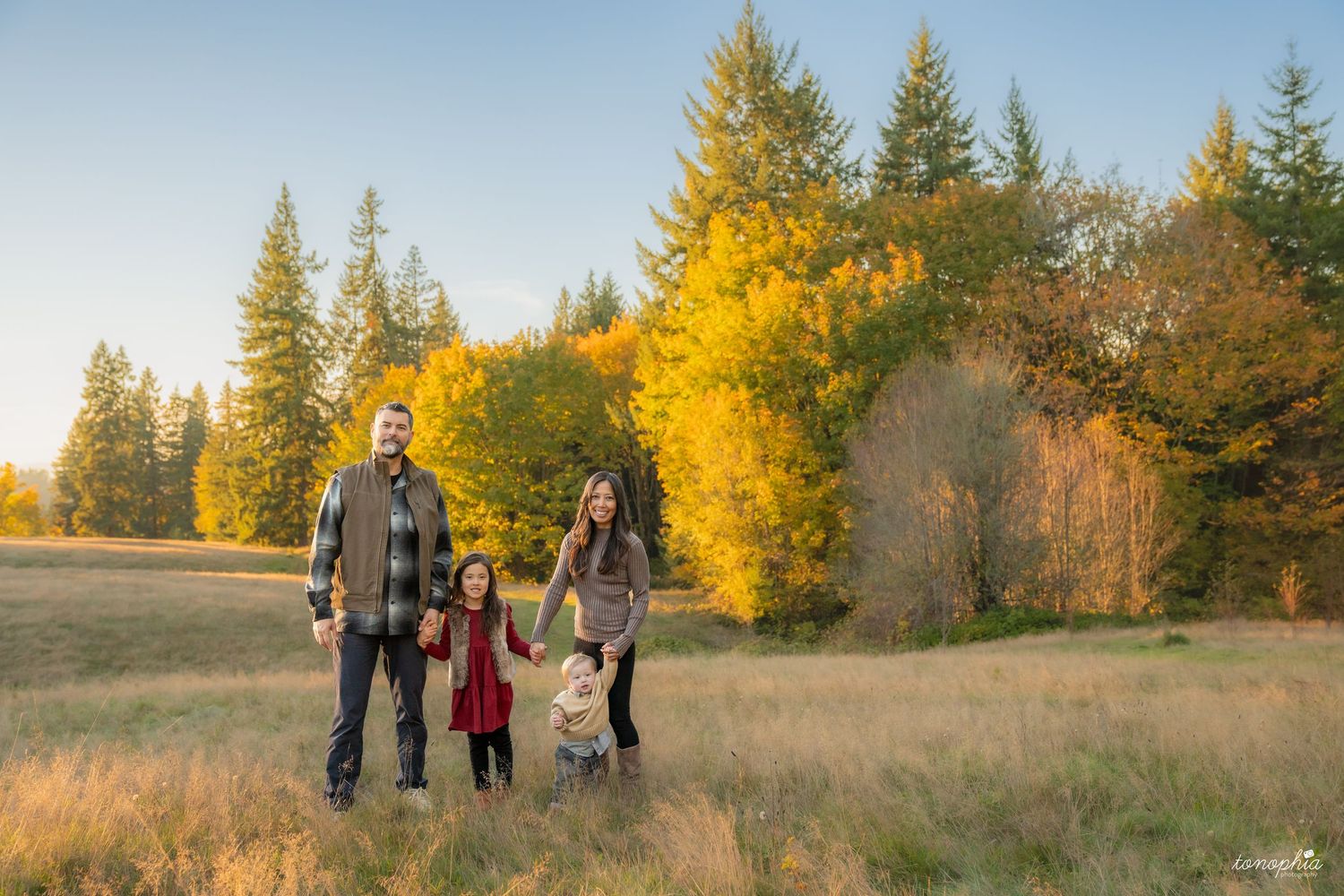 People stroll through a scenic autumn landscape with evergreen trees and golden foliage.
