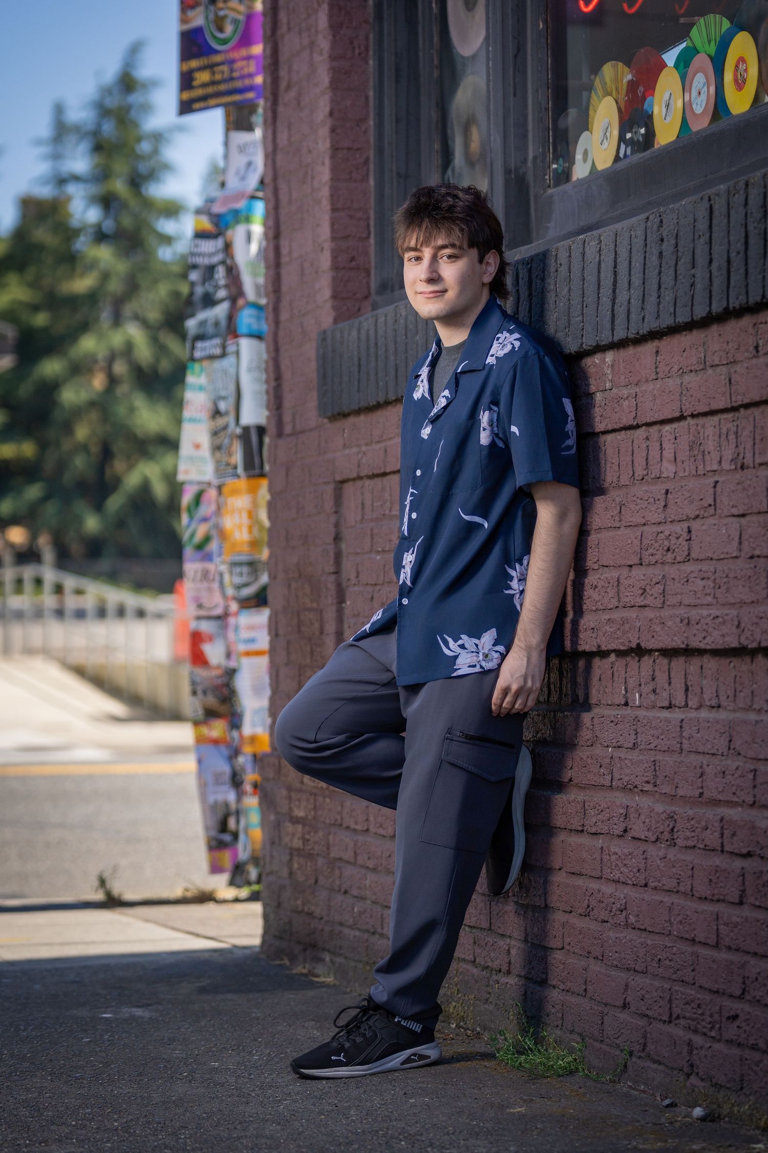 Person in navy blue outfit leaning against brick wall with colorful posters.