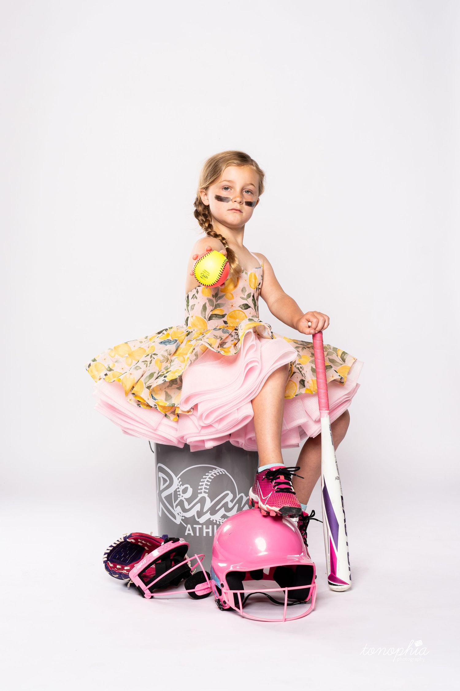 Young dancer posing with pink scooter wearing floral dress against white background.