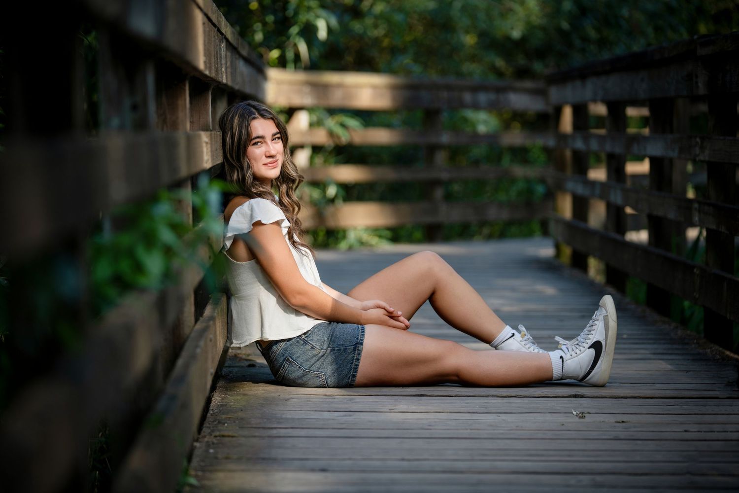 Relaxed pose on wooden boardwalk surrounded by greenery.