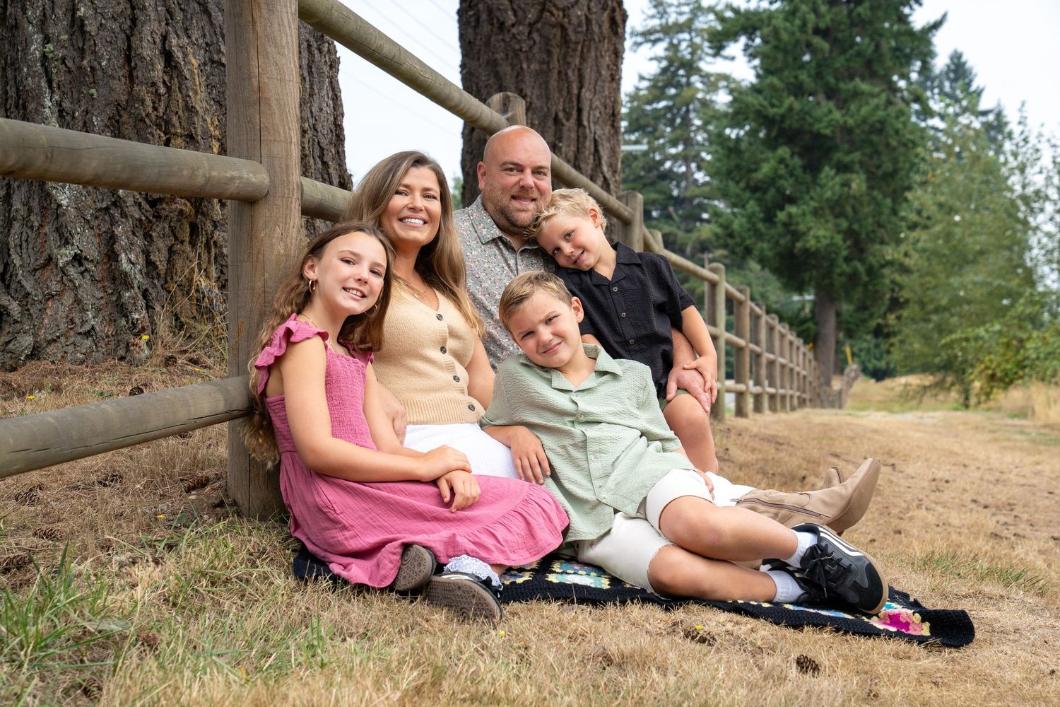 Family relaxing together on fallen logs in a wooded area during an autumn photoshoot.