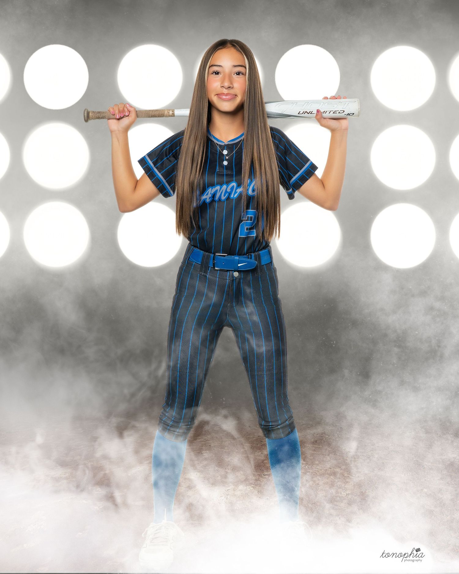 Softball athlete in blue pinstriped uniform poses with bat against dramatic lighting.