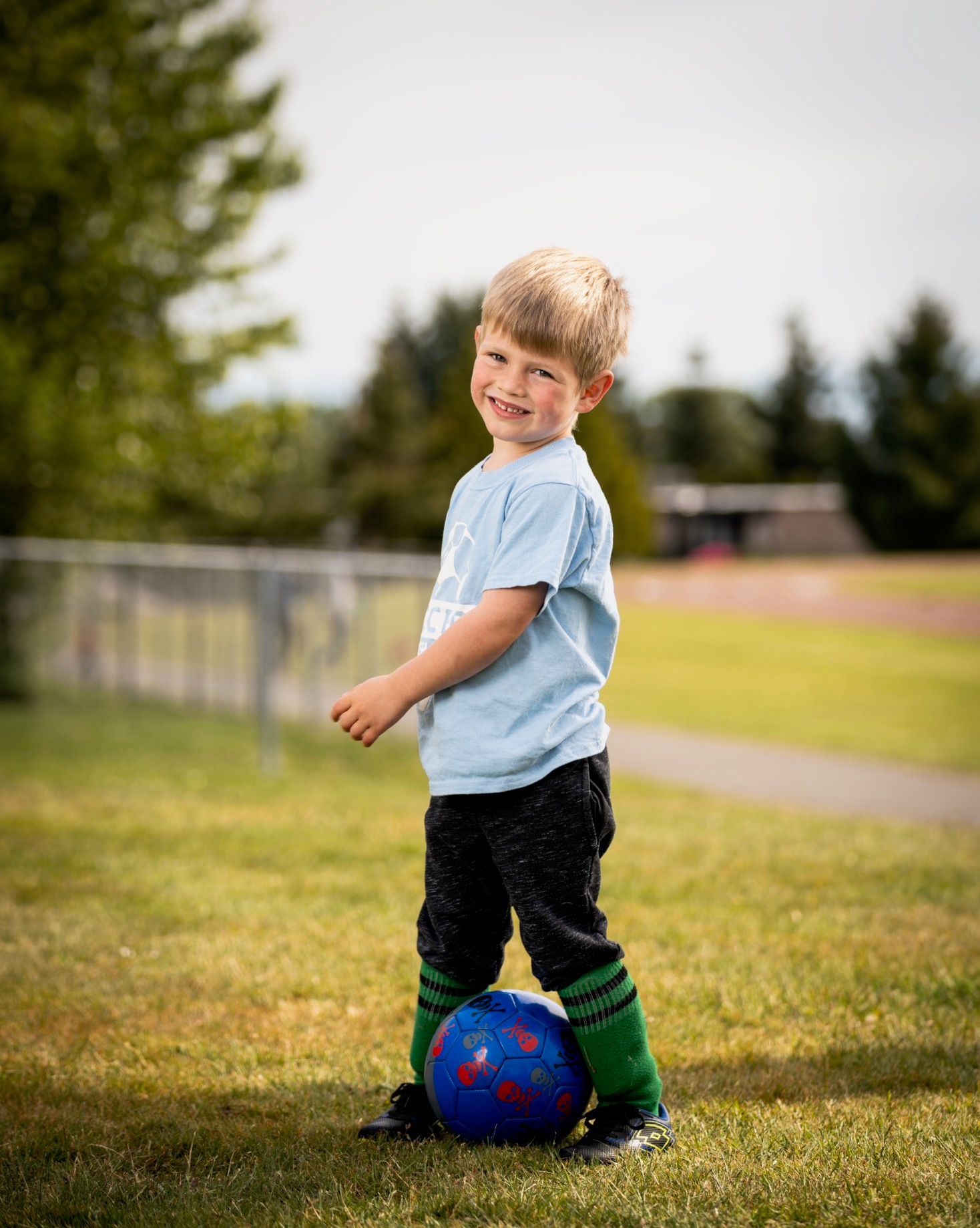 A child plays outdoors on a grassy field with a soccer ball on a sunny day.
