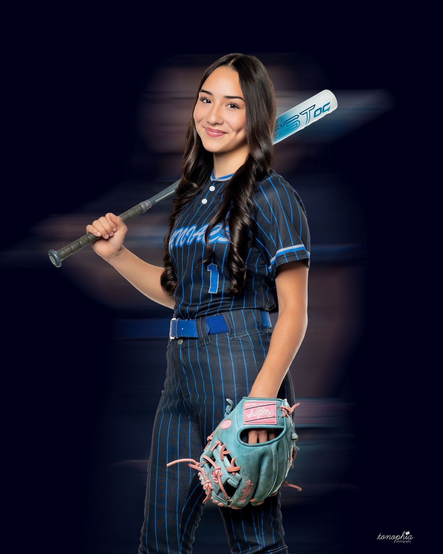 Baseball player poses in navy pinstriped uniform with bat and glove against dark background.