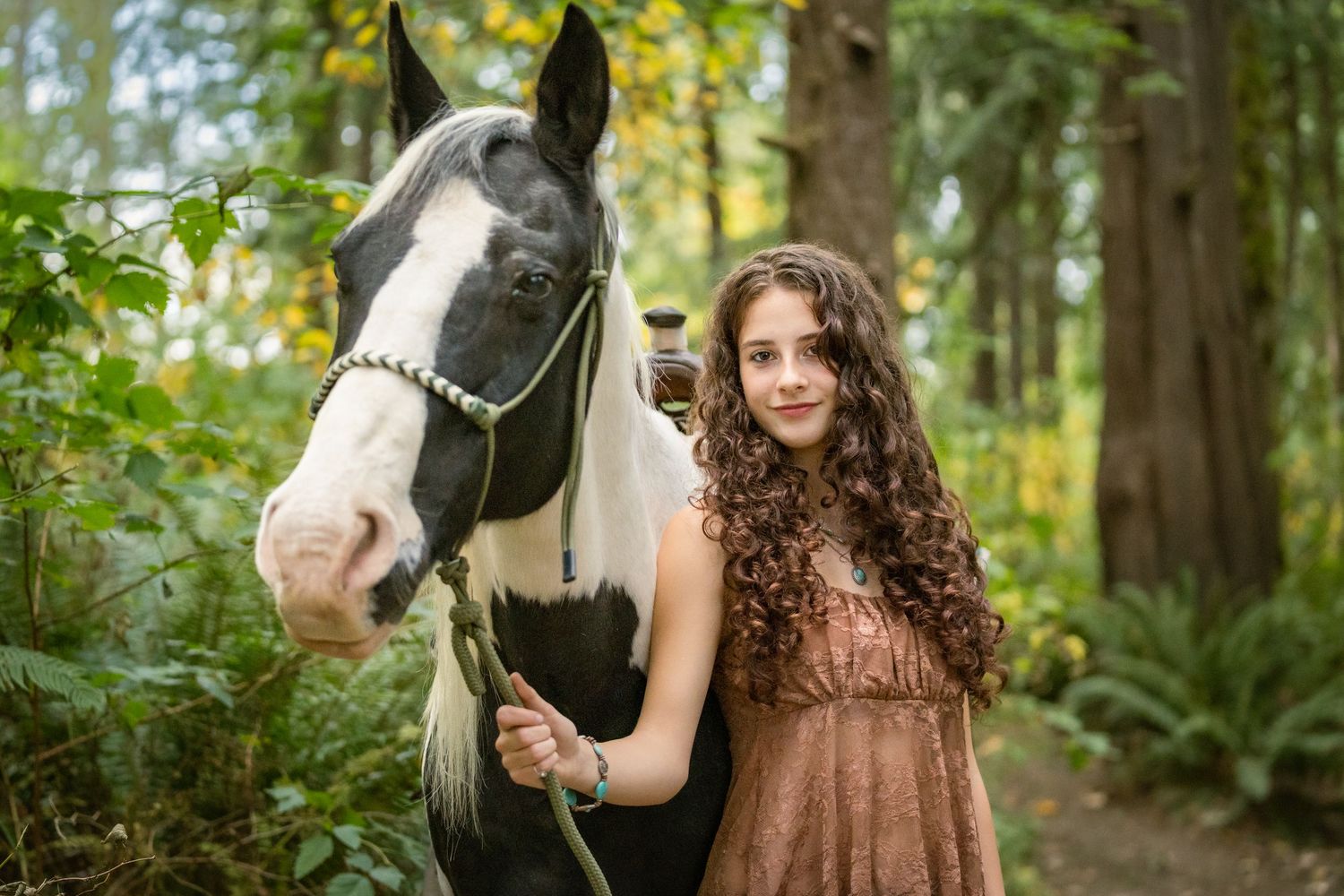 Horse and rider pose together in a wooded setting with autumn foliage.
