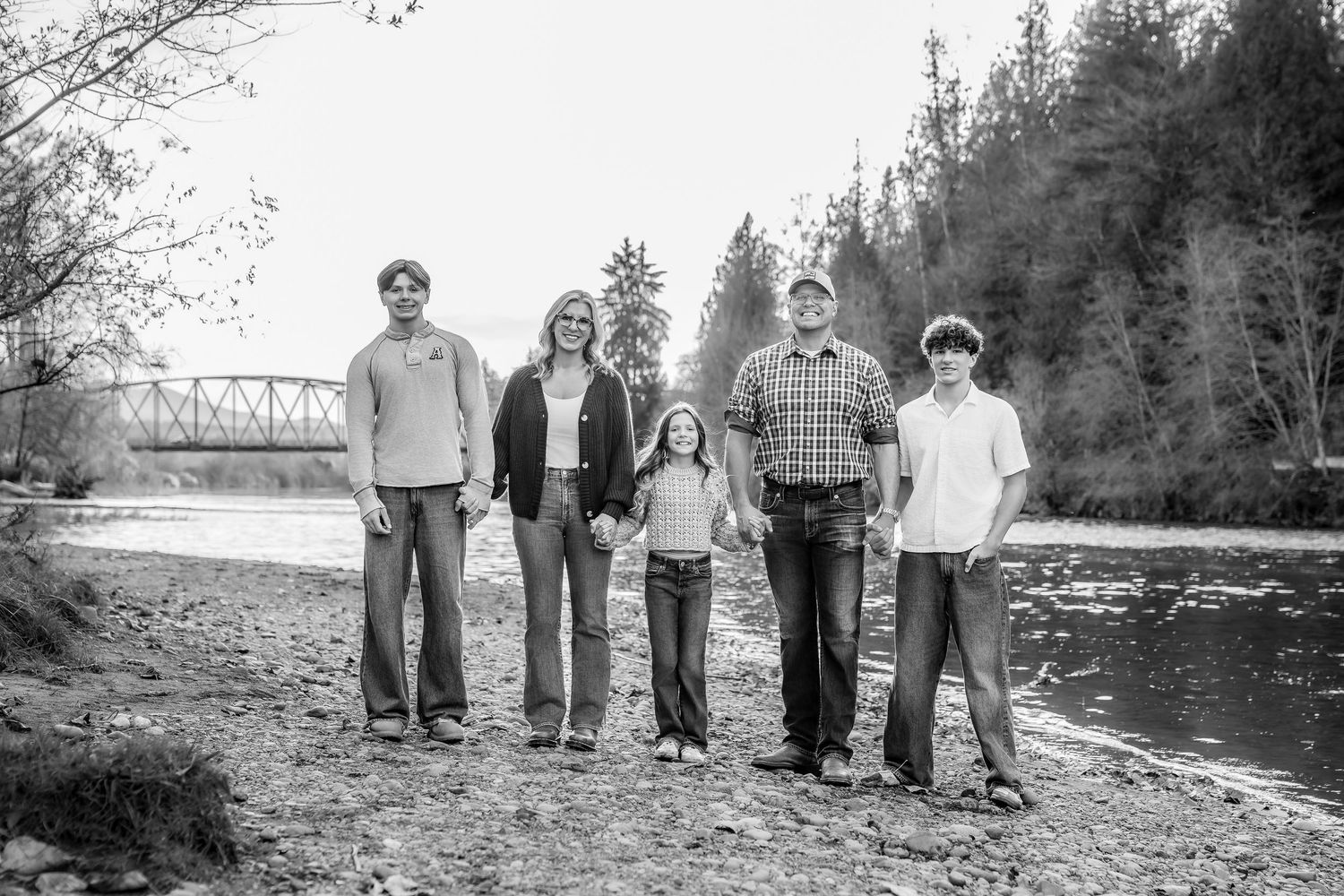 Black and white portrait of group on riverbank with trees and bridge in distance.