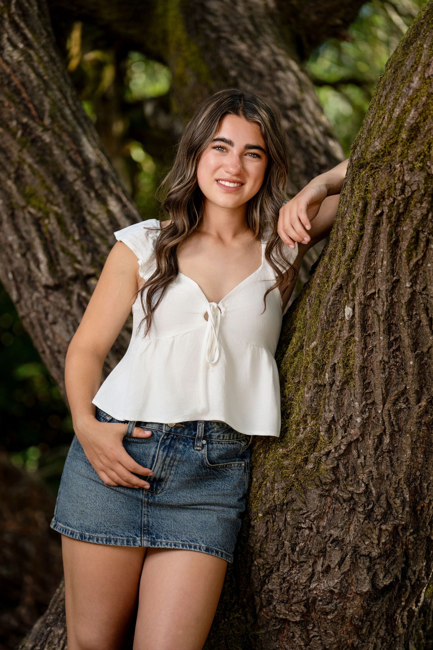 White top and denim shorts outfit posed against tree trunk backdrop.