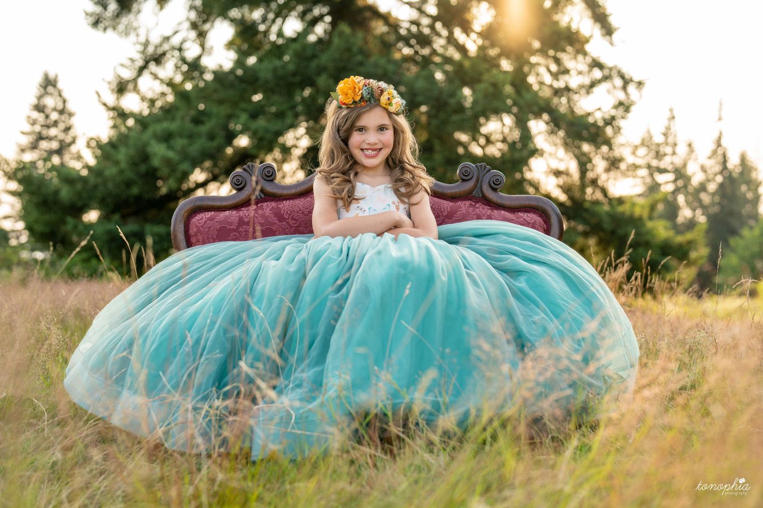 Two flowing gowns in turquoise and pink catch the golden sunlight in a grassy meadow at sunset.