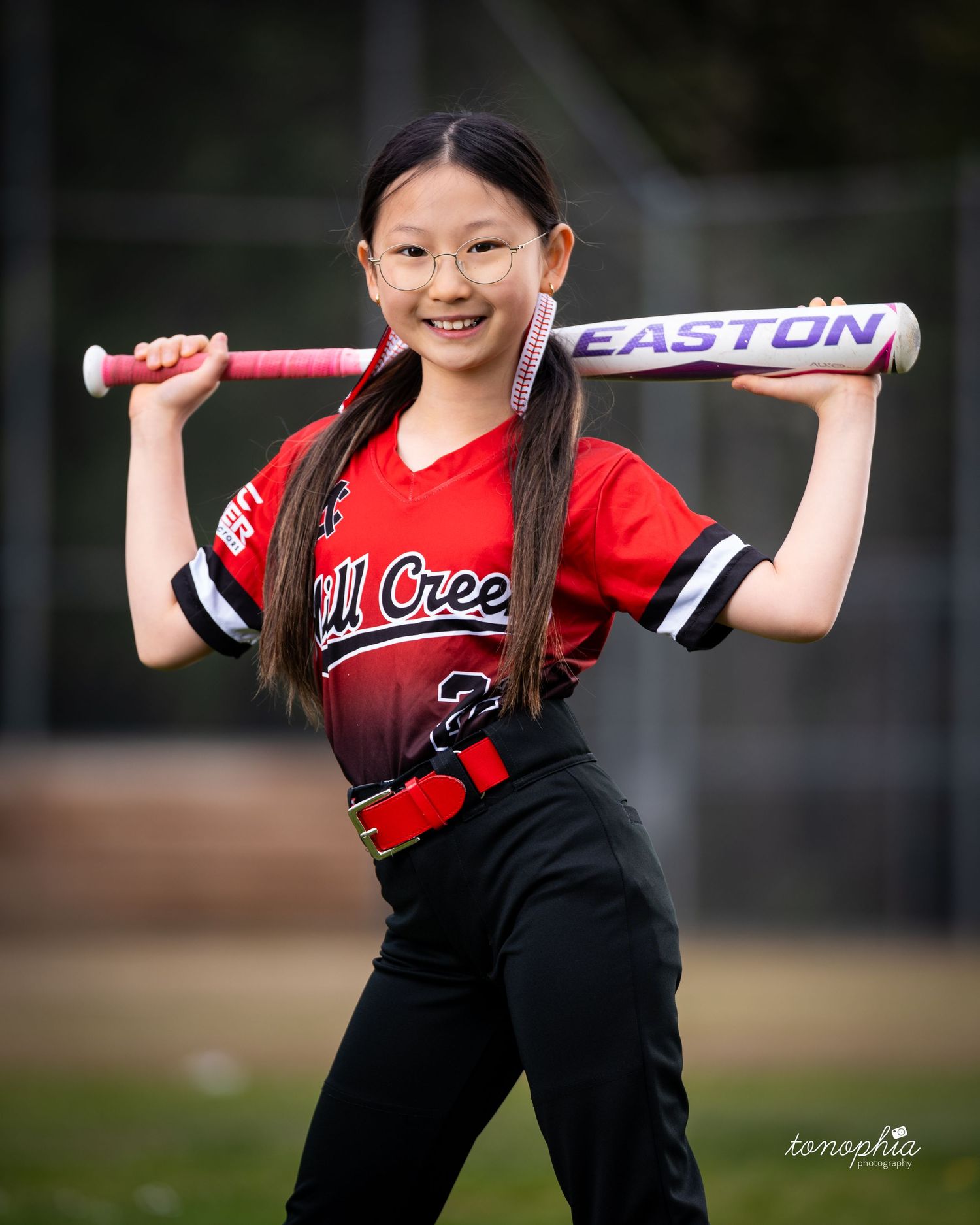 A softball player in red and black uniform holds an Easton bat during practice.