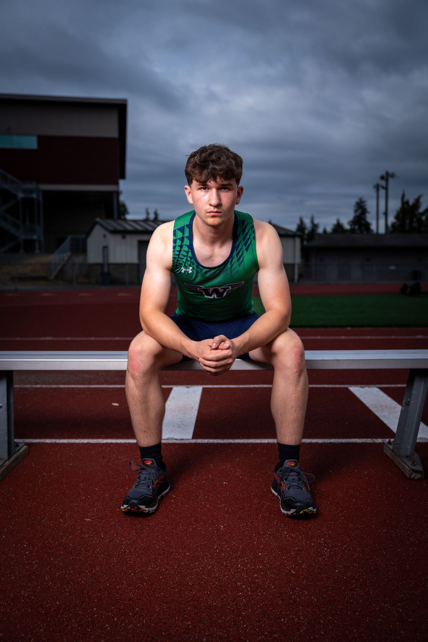 Athletic figure sits on red track surface against dramatic cloudy sky.