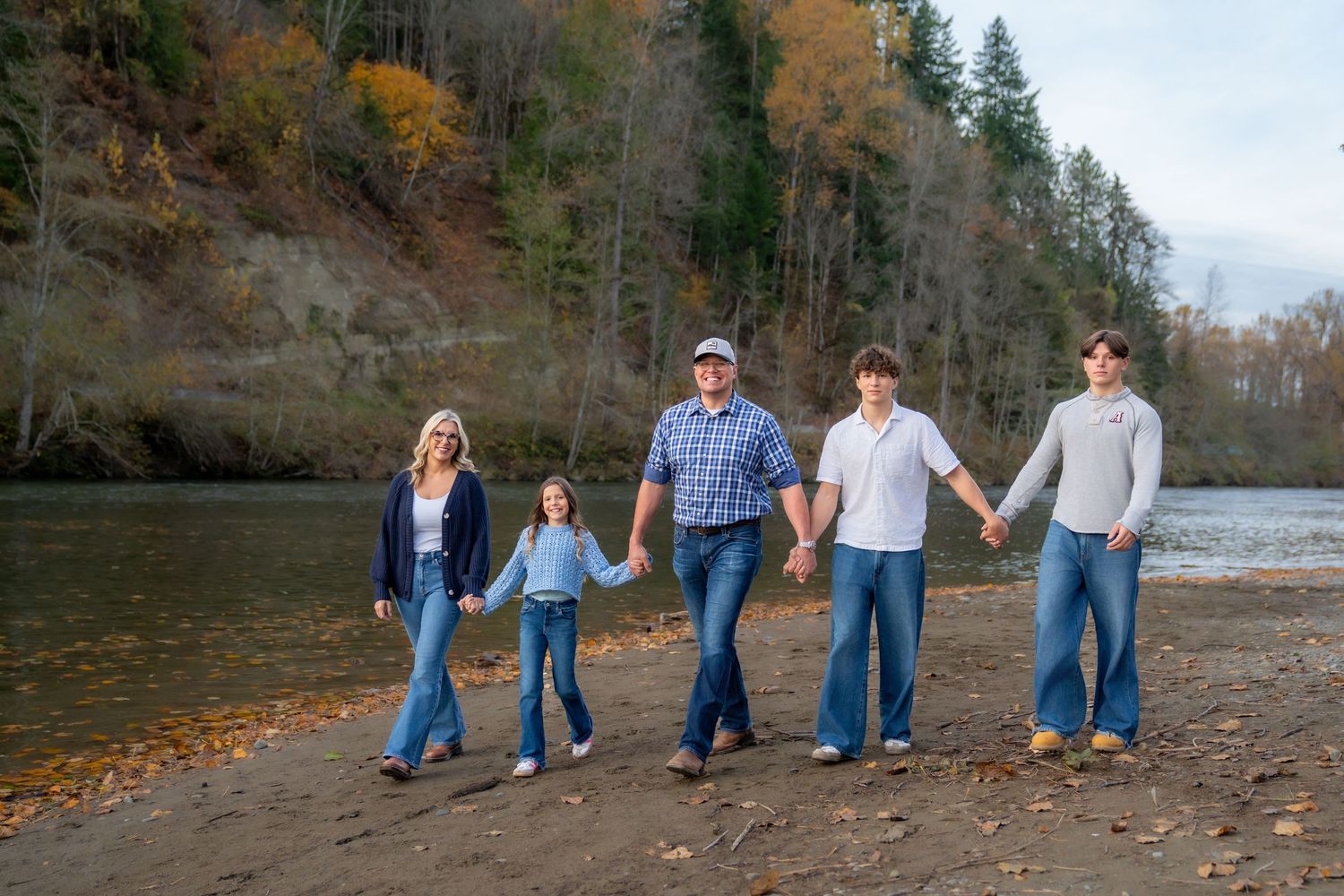 Group walking along rocky riverbank with autumn trees and water in background.